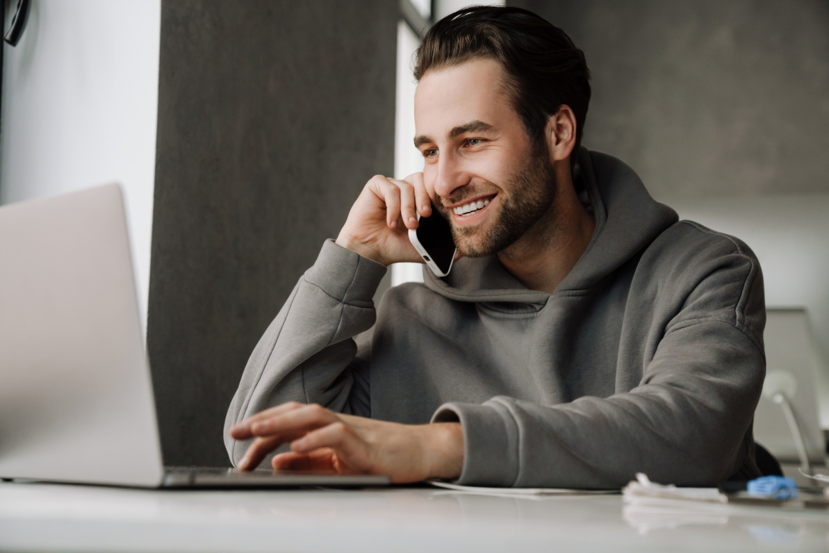 Young beard man talking on cellphone while working with laptop in office